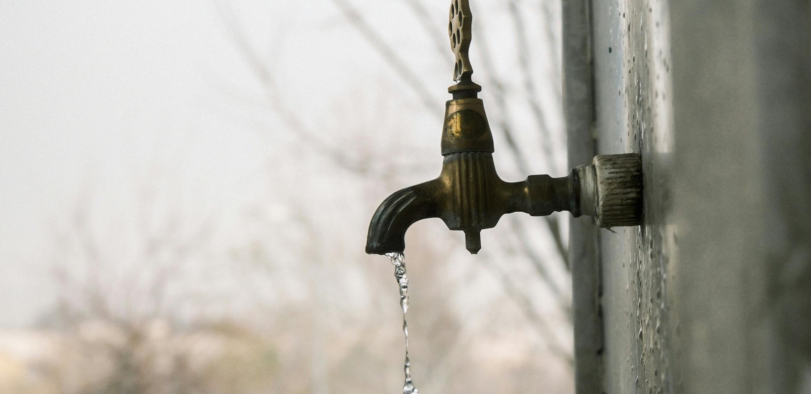 An outdoor faucet dripping water on a cold, gray day
