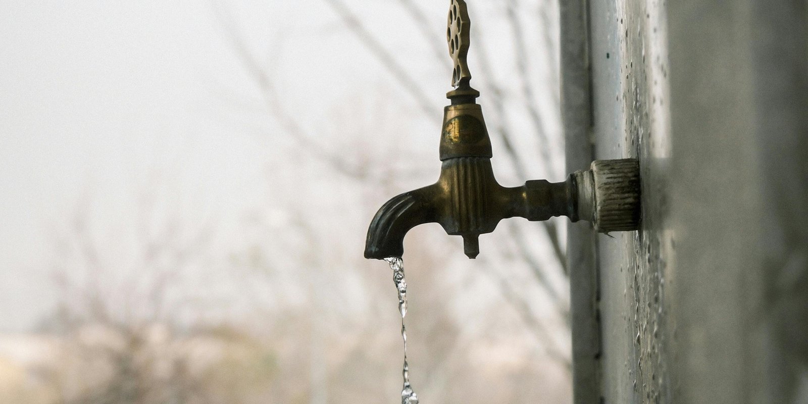 An outdoor faucet dripping water on a cold, gray day
