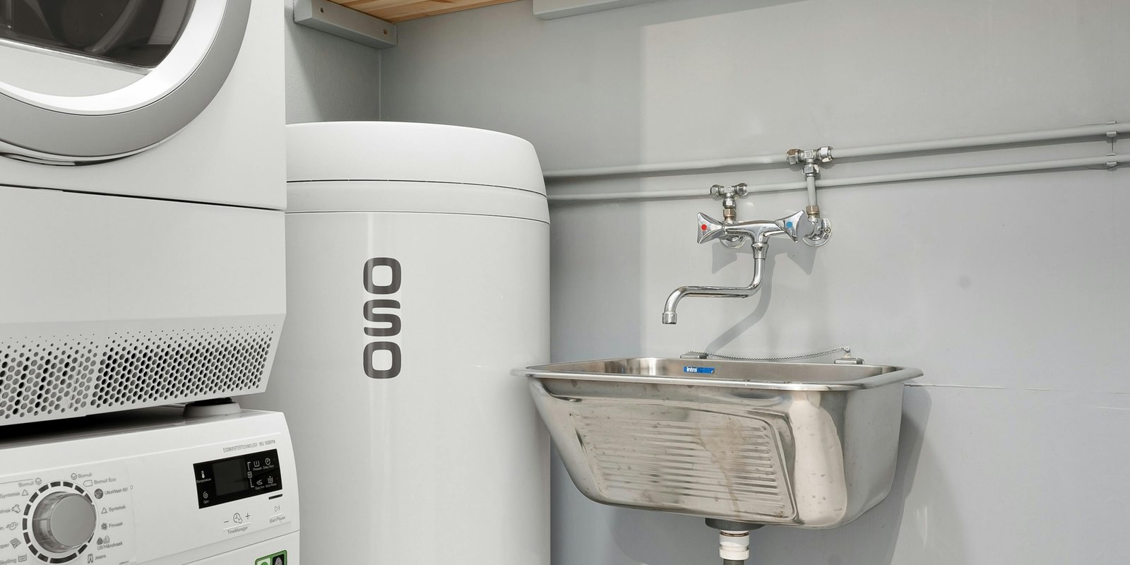 A white tank water heater in a laundry room, with the drain valve near the bottom